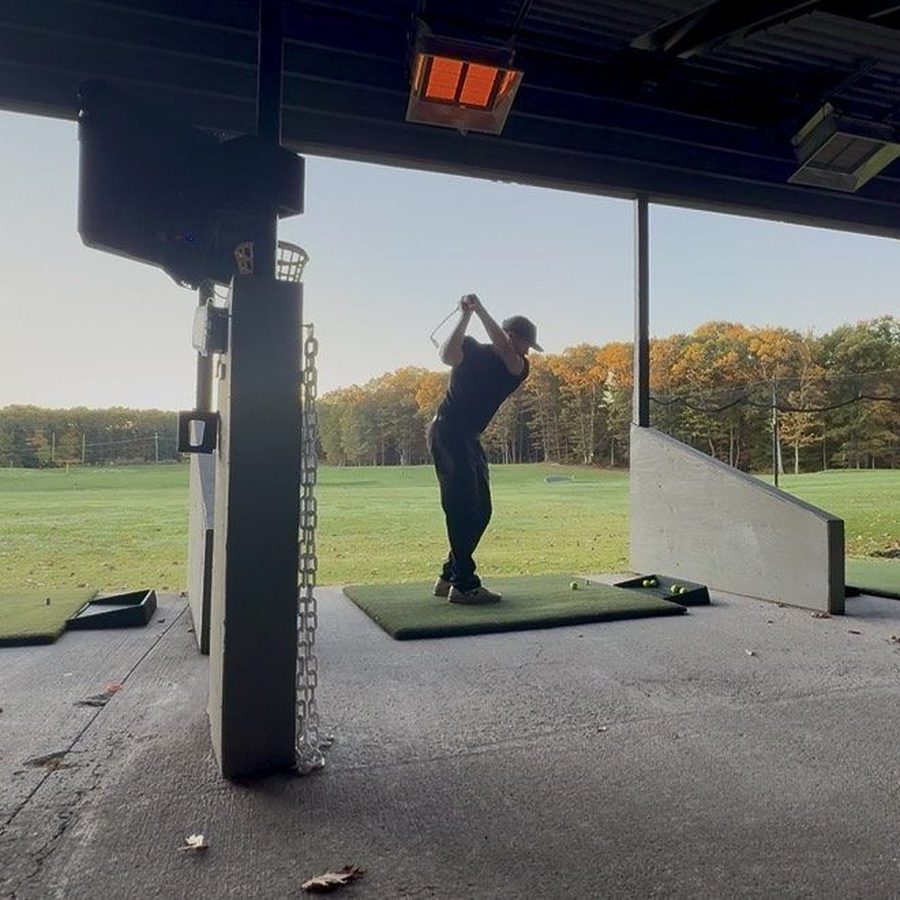 Golfer hitting from a covered bay under a glowing infrared heater at Southborough Golf Center